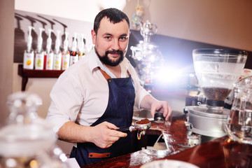 a handsome, bearded barista man holding a Holder with ground coffee. Making coffee in a coffee house