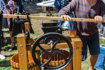 Young man is making apple juice using the big lever of an old fashion apple press, as part of a...