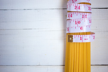 Measuring tape,diet theme. with bunch of uncooked Italian pasta spaghetti on the white wooden background. Diet, healthy food concept