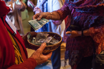 Woman with colorful clothes is putting 10 canadian dollars into a basket as voluntary contribution after a show - Closeup picture with a man in red shirt holding the basket - obrazy, fototapety, plakaty