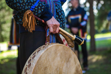 Woman in ceremonial clothing is holding her sacred drum as part of a community ritual out in the...