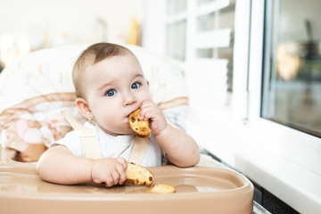 Baby girl eating cracker with raisins in a chair