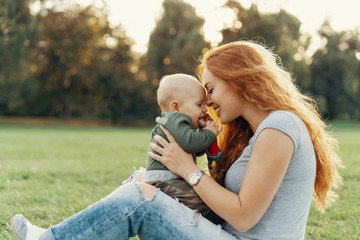Mother holds her son on her knees while playing on the grass