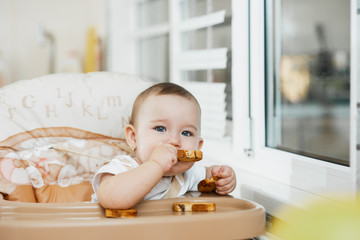 Baby girl eating cracker with raisins in a chair