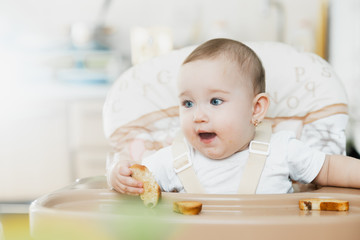 Fototapeta premium Baby girl eating cracker with raisins in a chair