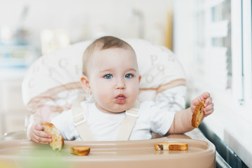 Baby girl eating cracker with raisins in a chair