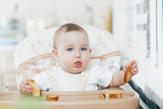 Baby Girl Eating Cracker With Raisins In A Chair