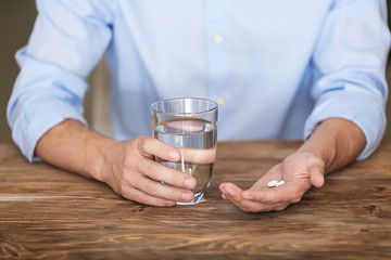 Fototapeta na wymiar Man holding pills and glass of water at wooden table, closeup