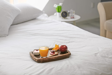 Fototapeta na wymiar Wooden tray with delicious breakfast on bed