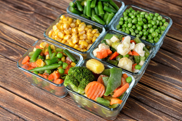 Glass bowls with frozen vegetables on wooden table