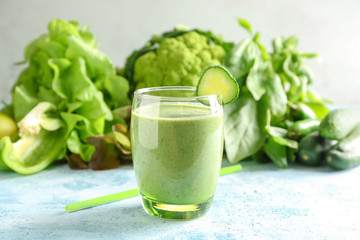 Glass of tasty green smoothie and ingredients on color table