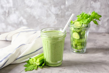 Jars with tasty green smoothie and cut vegetables on grey table