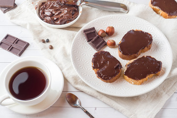 Sandwiches with chocolate hazelnut spread on the plate. Cup of coffee on the table.