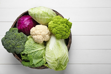 Wicker basket with different kinds of cabbage on white wooden table