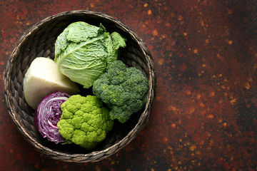 Wicker basket with different kinds of cabbage on color table