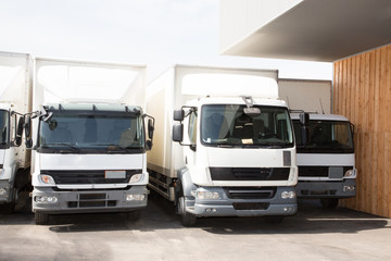 four white trucks ready for delivery in front warehouse in sunny day