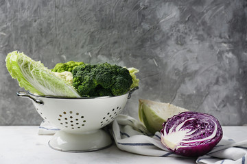 Colander with different kinds of cabbage on white table