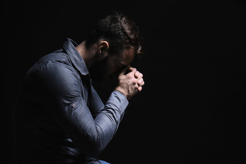 Religious young man praying to God on black background - obrazy, fototapety, plakaty