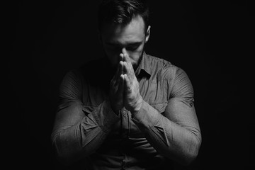 Religious young man praying to God on dark background, black and white effect