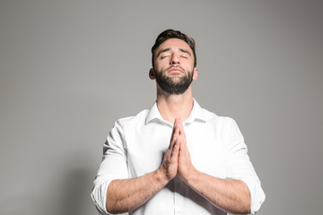 Religious young man praying to God on light background