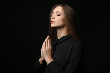 Beautiful young woman praying on dark background