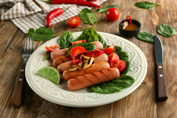 Plate with delicious grilled sausages and vegetables on wooden table
