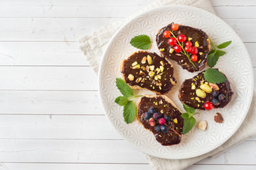 Sandwiches with chocolate paste, pistachio nuts and fresh berries on a plate. Copy space