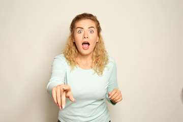 Portrait of shocked young woman pointing at viewer on light background