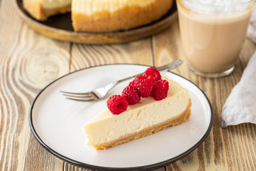 Piece of classic cheesecake with raspberries and coffee on a wooden background. Copy space.