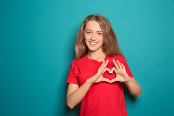 Portrait of beautiful young woman making heart with her hands on color background