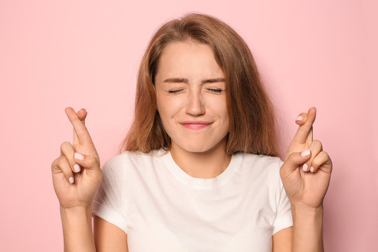 Portrait of emotional young woman with crossed fingers on color background