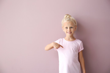 Cute little girl pointing at her t-shirt on color background