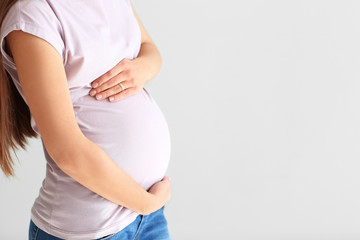 Young pregnant woman on light background