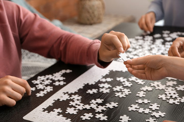 Group of people assembling puzzle on dark table