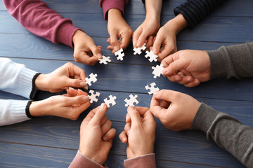Group of people holding pieces of puzzle over wooden table