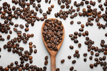 Spoon and scattered coffee beans on white background