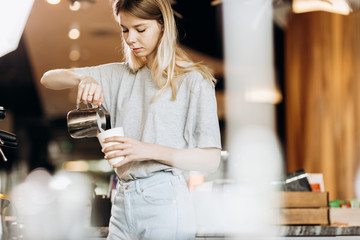 A good looking slim blonde with long hair,dressed in casual outfit,is cooking coffee in a modern coffee shop. Process of making coffee is shown.