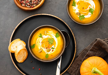 Pumpkin soup in a bowl with fresh pumpkins, garlic and parsley herbs on a black background. Autumn concept.