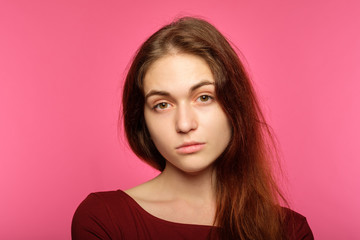 young beautiful girl with a poker face. lack of emotion. portrait of indifferent cold icy nonchalant woman on pink background.