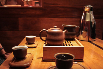 3 people tasting and drinking very dark pu-erh tea into small tasting cups - 2/2 - Shot during a gong fu cha tea ceremony with a very small teapot on a tea boat, placed on a wooden table