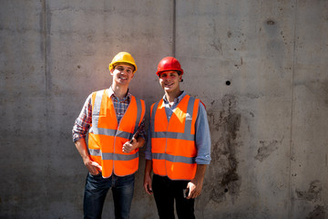 Structural engineer and architect dressed in orange work vests and  helmets stand on a concrete wall background