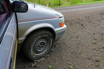 Fototapeta na wymiar Grey van has its tires full of clay from driving on a wet clay road - 2/2 - Closeup picture on the front right wheel of the vehicle, fully surrounded by a thin layer of clay