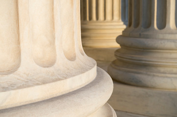 Lower detail of classical fluted columns in a colonnade in white marble lit by soft golden sunlight