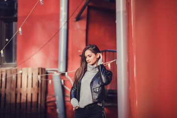 Portrait brunette woman wearing a black rock leather jacket against the colorful red wall
