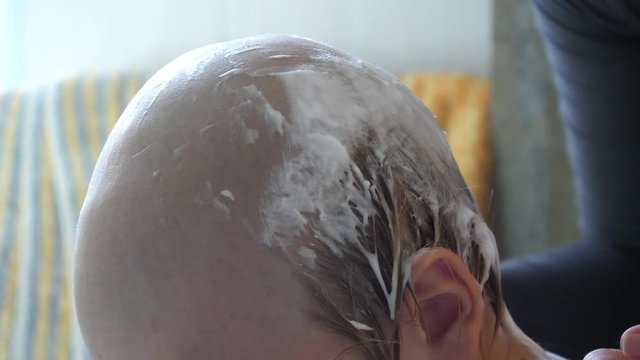 Young mother shaves head of blond boy with razor for preventing pediculosis. Good family tradition. Child is happy from hygiene procedures.