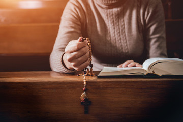 Obraz premium Christian woman praying in church. Hands crossed and Holy Bible on wooden desk.