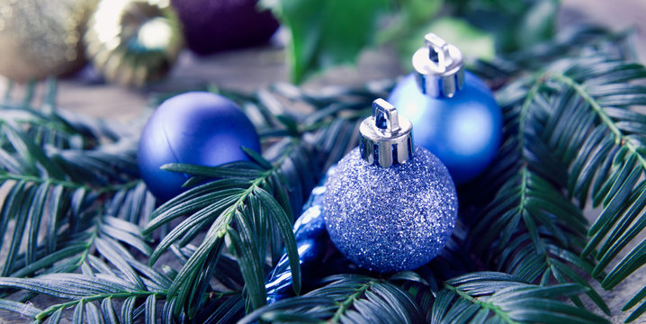 Blue, frozen, gold,  silver Christmas decor small baubles decorations with holly tree leaves and wooden rustic background.