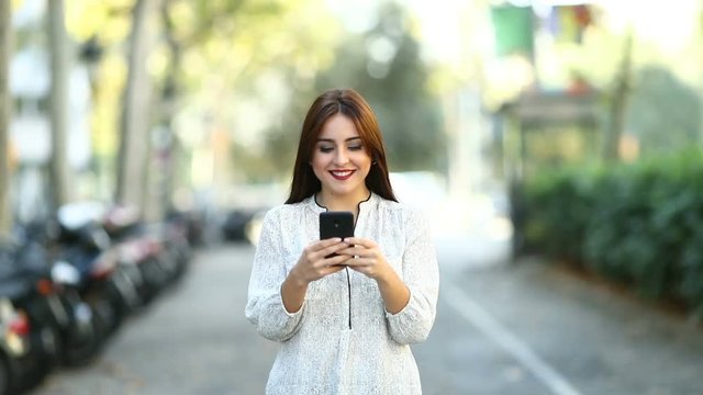 Front view of a happy woman walking and using a smart phone in the street recorded in slow motion