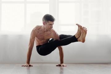 Fit muscular flexible man posing in difficult yoga pose