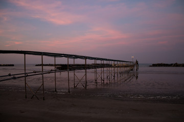 Peaceful evening on the shore, with scenic pink sunset reflected on water ant metallic pier; adriatic sea